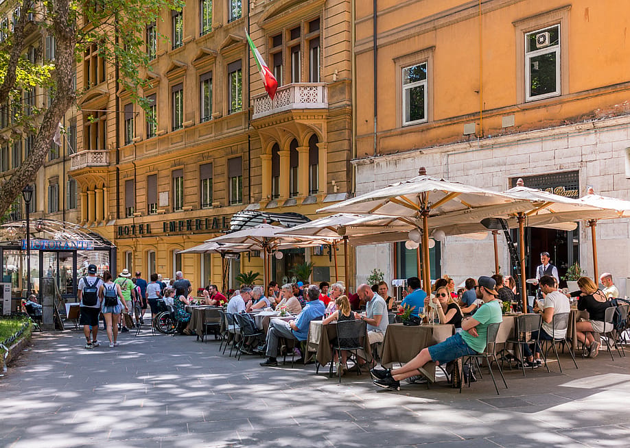 Tables under umbrellas filled with people outside of restaurants in Rome. — Boris-B // Shutterstock