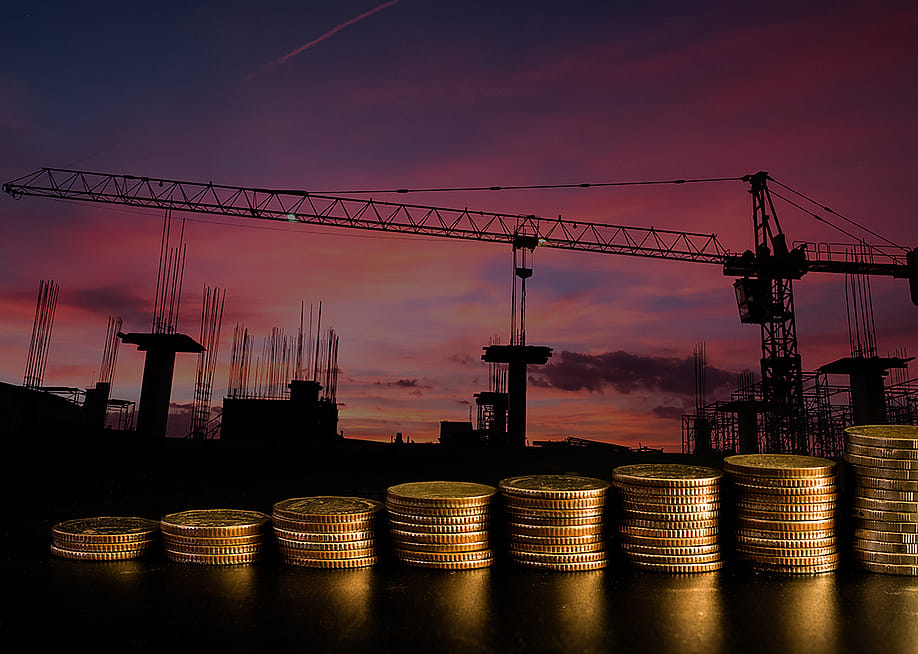 A row of stacked coins with an estate construction site background. — Pisit.Sj // Shutterstock
