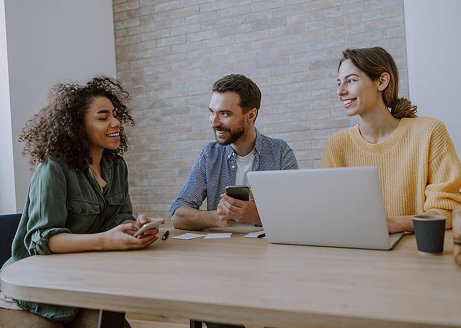 A 3-member creative team engaged together in a discussion in an office. — Yaroslav Astakhov // Shutterstock