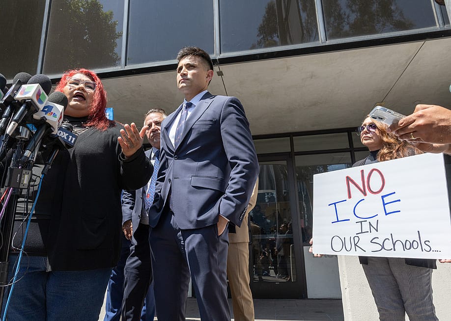 Andreina Mejia, mother of the Arleta High School student, a citizen, who was detained by immigration agents, speaks about their experience at a press conference announcing legal claims against the U.S. government. A few people stand beside her, including one woman holding a sign that reads, "No ICE in our schools." — Myung J. Chun // Los Angeles Times via Getty Images