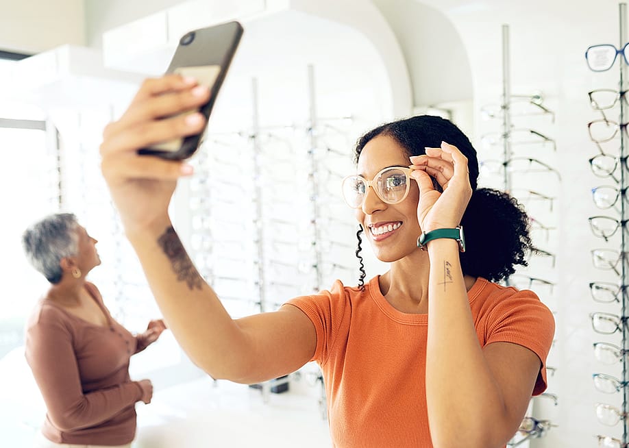 A young woman trying on eyeglasses in a shop and taking a selfie. — PeopleImages // Shutterstock
