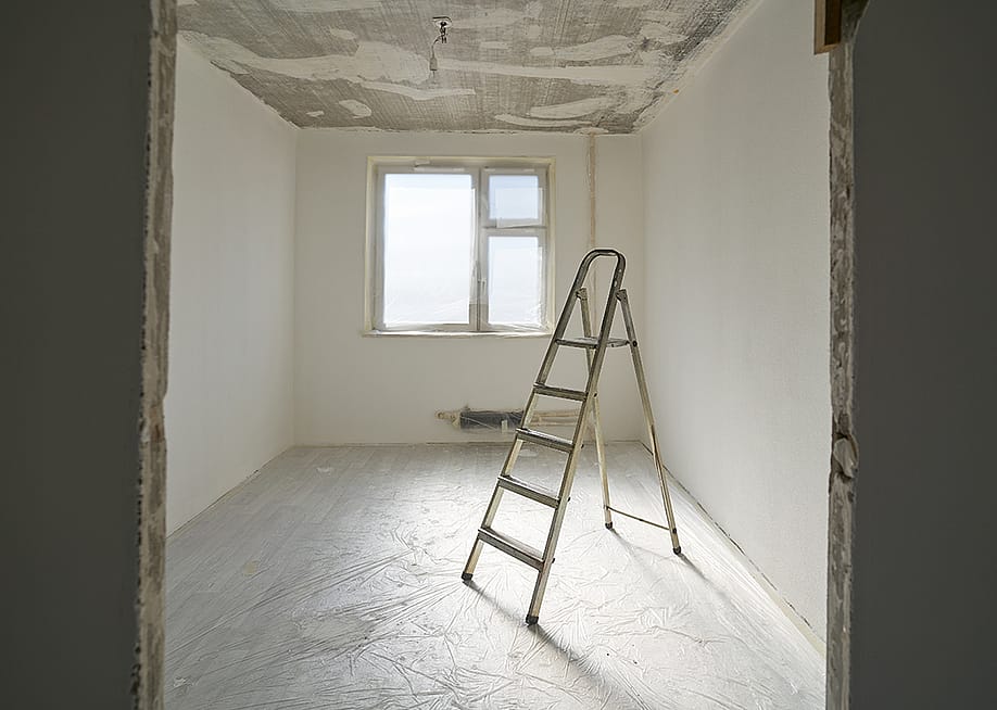 A ladder at the center of an apartment room with unfinished interior paint. — nuclear_lily // Shutterstock