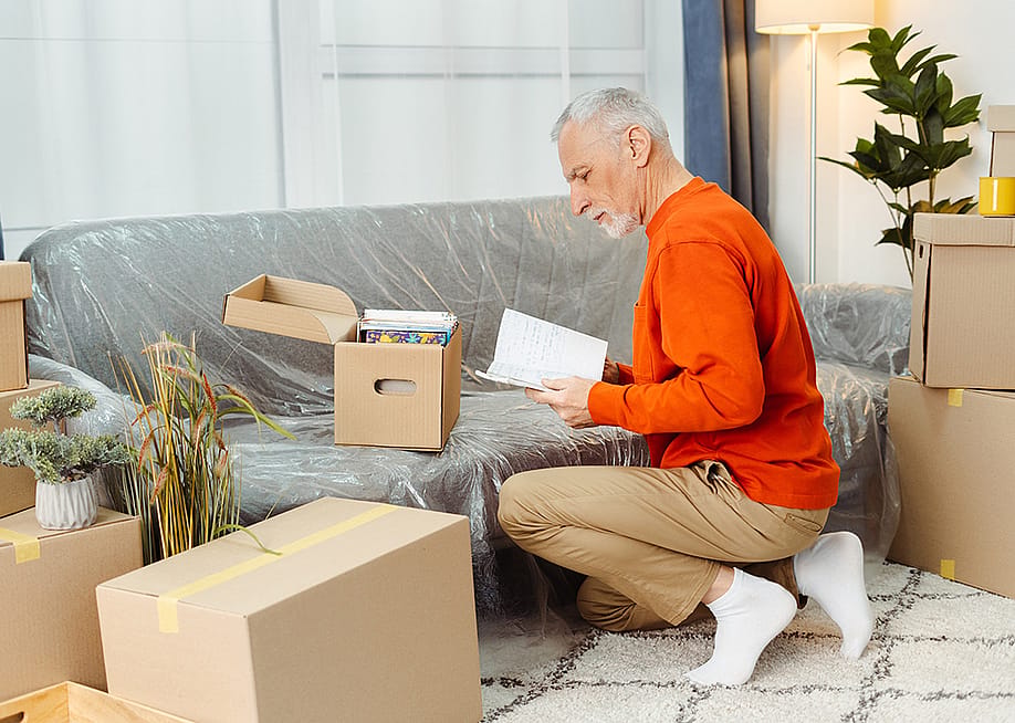 A senior man unpacking boxes of belongings when moving to a new home. — AYO Production // Shutterstock