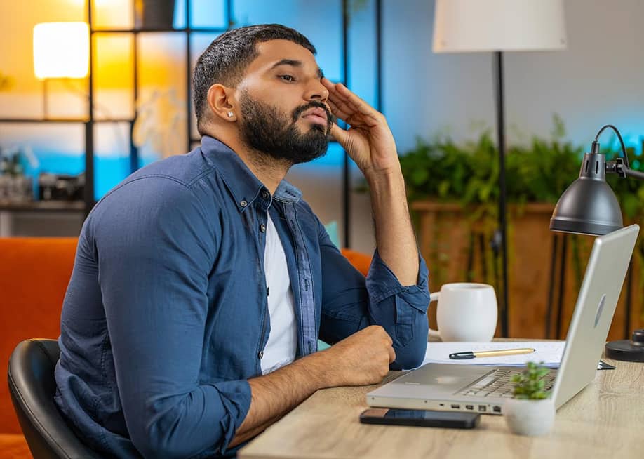 Man sitting at desk in modern colorful room looking at computer with an expression of distrust. — Andrii Iemelianenko // Shutterstock.