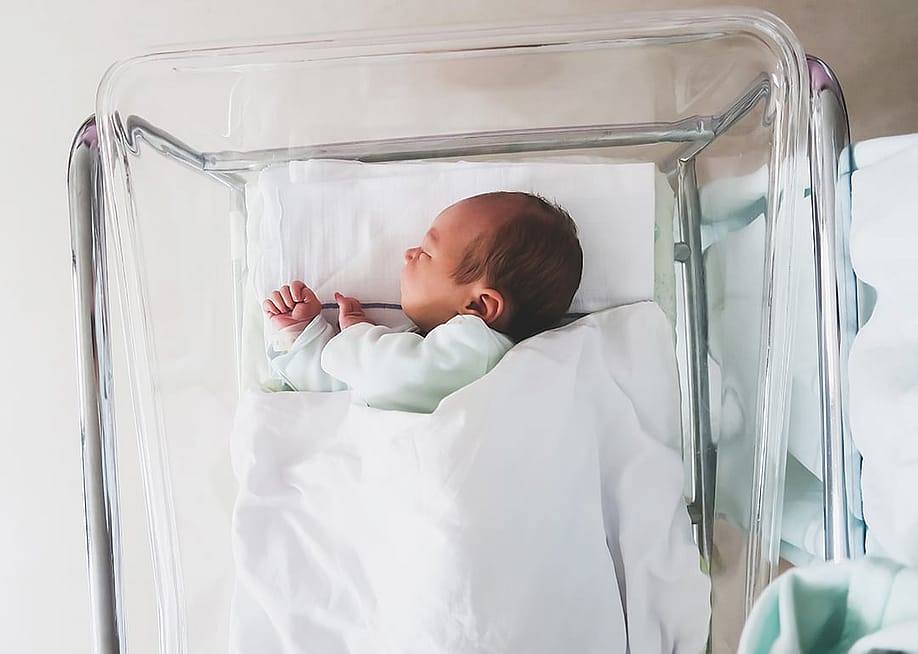 A newborn baby sleeping in a hospital crib. — Natalia Deriabina // Shutterstock