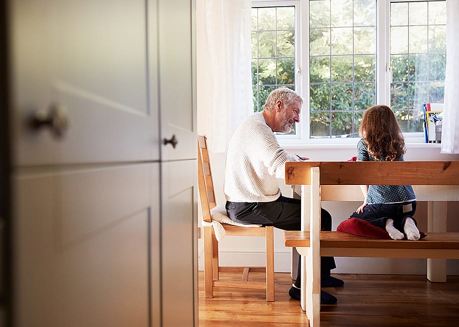 A grandfather and his granddaughter in the dining room doing a coloring activity together. — Monkey Business Images // Shutterstock