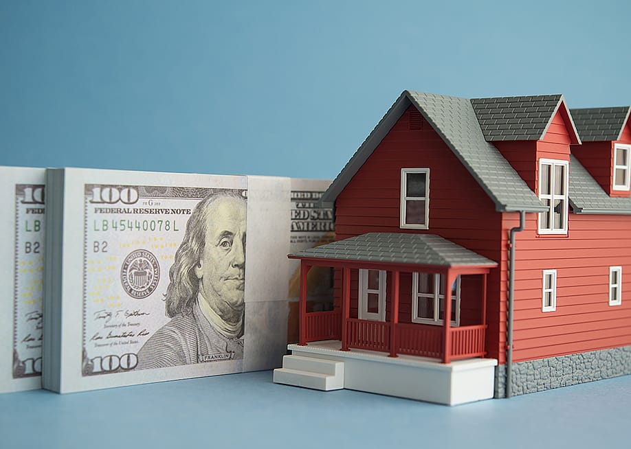 US dollar banknotes and a figure of a home. — Pla2na // Shutterstock