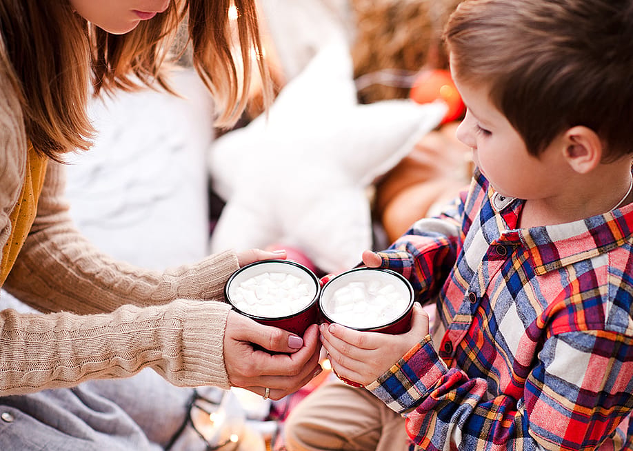 A young boy holding a cup of hot chocolate with his mother. — morrowlight // Shutterstock