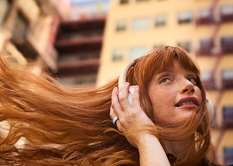 A woman's red hair flowing as she listens to her headphones outdoors. — Oura