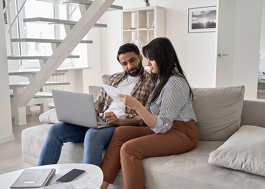 A couple sitting together on a sofa and reviewing bills. — Ground Picture // Shutterstock
