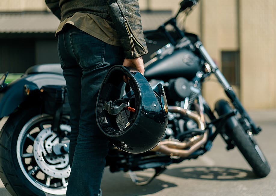 Close up of person holding motorcycle helmet with Harley type motorcycle in the background. — guys_who_shoot // Shutterstock