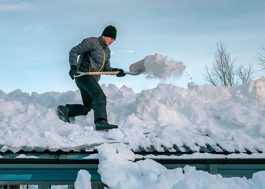 Young person shoveling heavy snow on a rooftop. — AlexDreamliner // Shutterstock