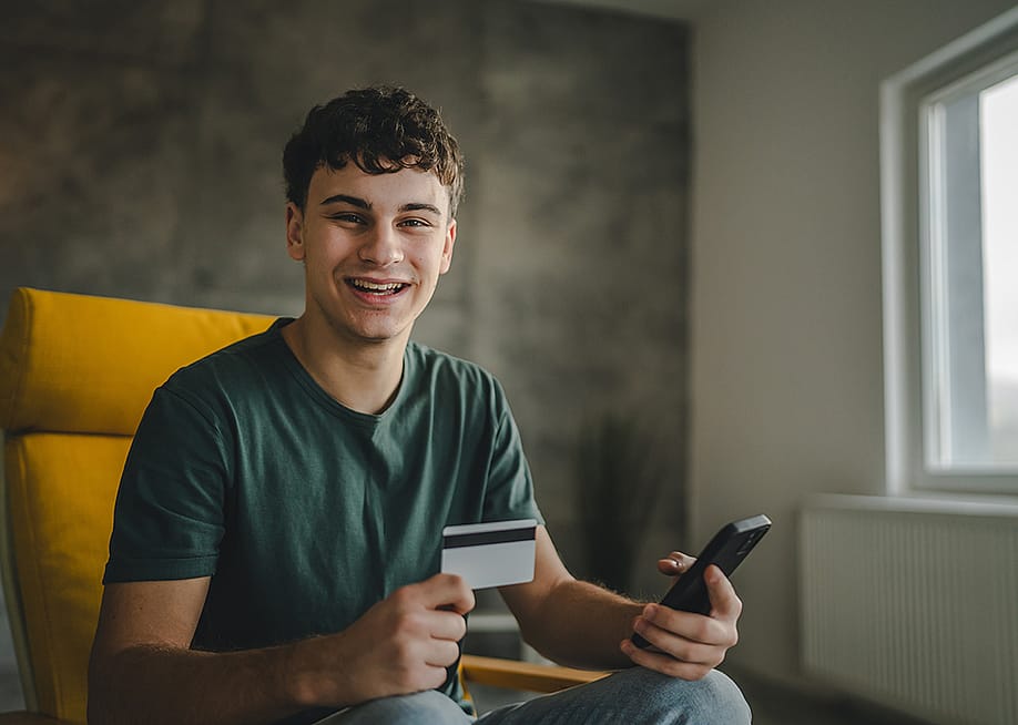A happy young man using a credit card to purchase online. — Miljan Zivkovic // Shutterstock
