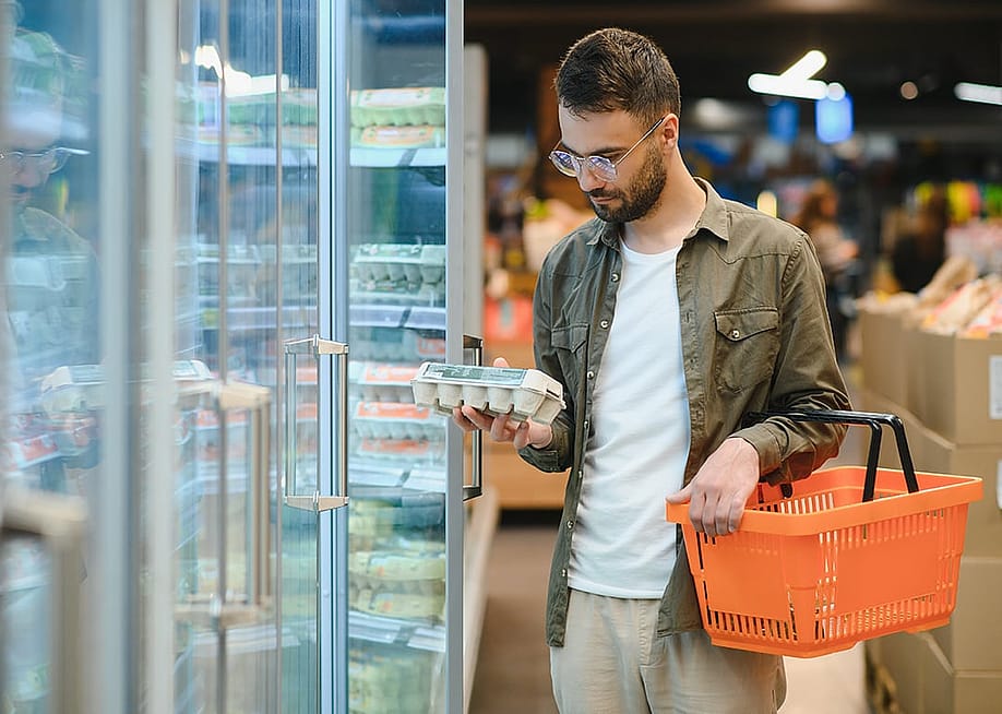 A young man checking eggs from a grocery store shelf. — Hryshchyshen Serhii // Shutterstock