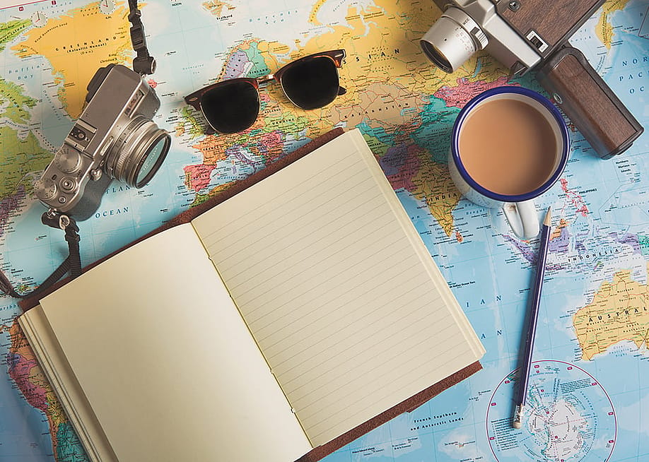 Traveller items such as a camera, sunglasses, and an empty planner on top of a world map. — Luke Holland // Shutterstock