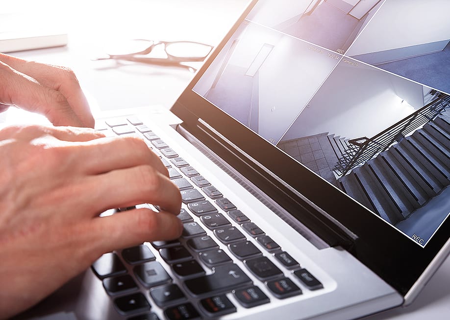 Person monitors a split screen view of CCTV footage using a laptop. — Andrey_Popov // Shutterstock
