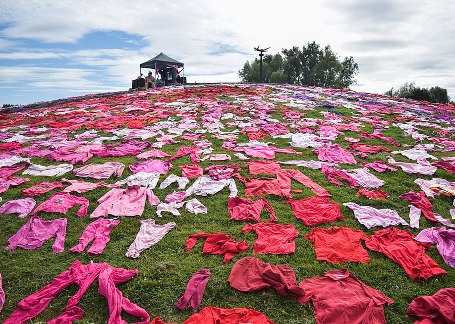 The XR Guerrilla Fashion's protest in Utrecht's Griftpark showcased a 7,000-garment installation by Pet van de Luijtgaarden. Red and pink clothing is laid out on a grassy field with a small tent of a few people in the distance. — MOUNEB TAIM / Middle East Images // AFP via Getty Images