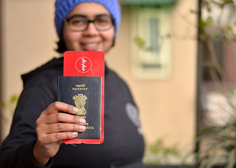 Portrait of a young Indian woman holding up her passport with an international flight ticket. — PhotographerIncognito // Shutterstock