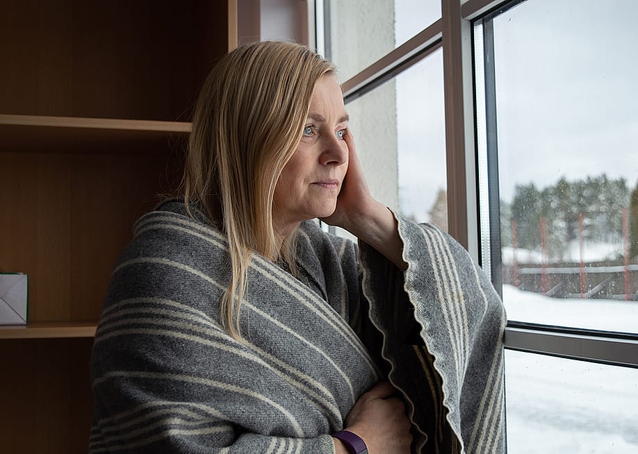 Woman wrapped in blanket looking out the window during winter. — Hellame // Shutterstock