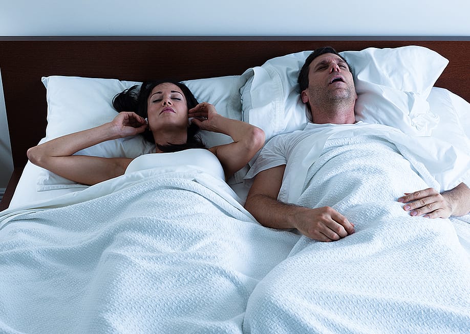 A couple sleeping in bed together where the wife is disturbed by her husband's snoring. — EHStockphoto // Shutterstock
