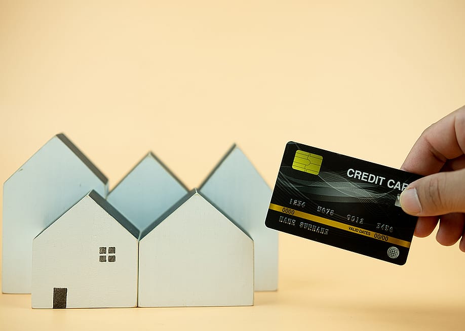 Hand holding a credit card over small figures of houses. — Dontree_M // Shutterstock