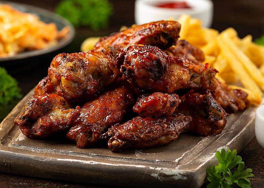 Buffalo chicken wings served on a wooden board with fries and other side dishes. — DronG // Shutterstock