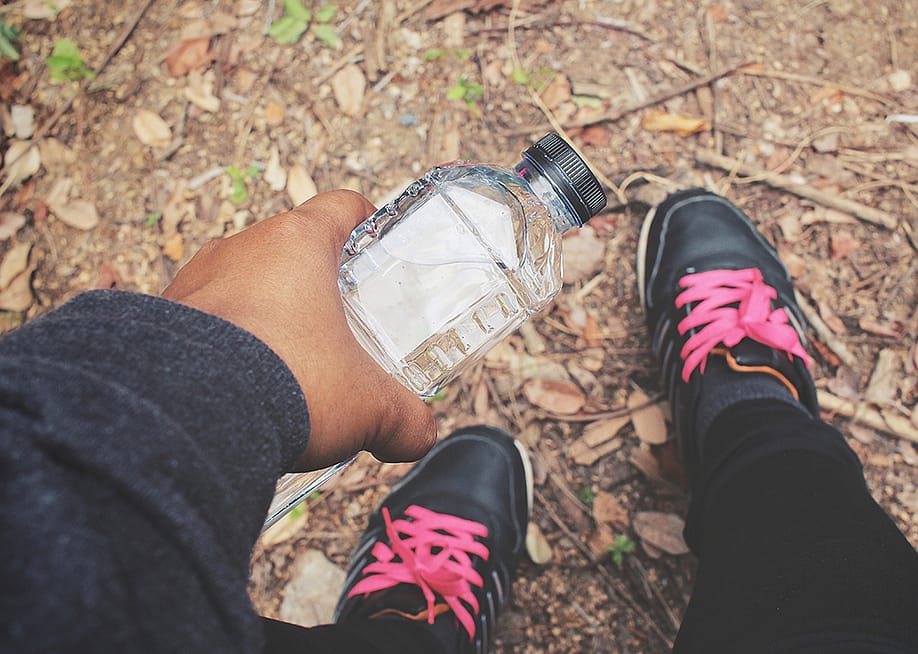 A selfie-style photo showing a person holding a water bottle and their fitness shoes while outdoors. — Mumumutelu // Shutterstock