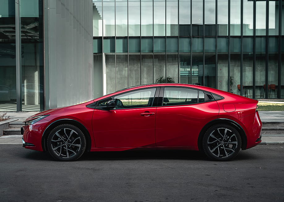A red 2024 Toyota Prius Prime parked in front of a building on a city street. — Gabriel Nica // Shutterstock