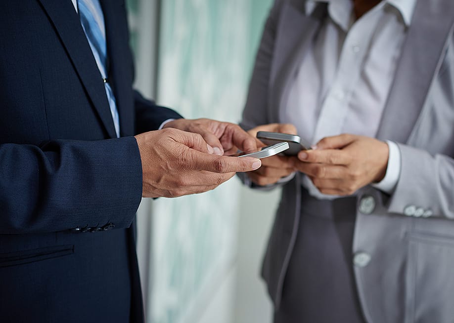 Two businesspeople on their phones exchanging numbers. — Dragon Images // Shutterstock