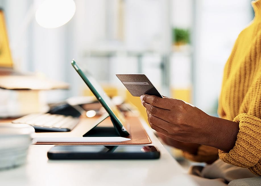 A businesswoman holding up a credit card while at work in the office. — PeopleImages // Shutterstock