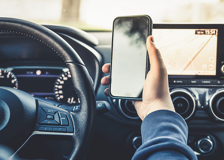Person's hand holding up a smartphone while driving. — Fabio Principe // Shutterstock