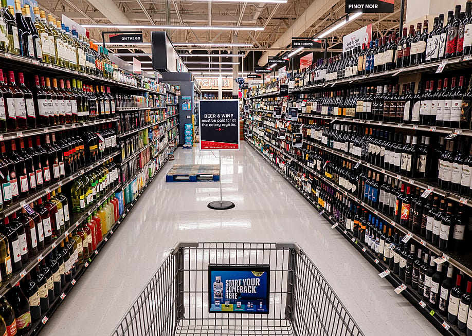 A shopping cart in a grocery store aisle filled with wine bottles. — Robert Hale // Shutterstock