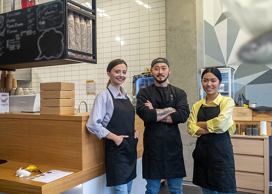A team of young cafe workers pose in front of their shop's front bar. — Dmytro Zinkevych // Shutterstock