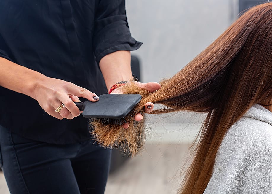 A professional hairstylist combing a client's hair with a paddle hairbrush. — Antonina Vlasova // Shutterstock