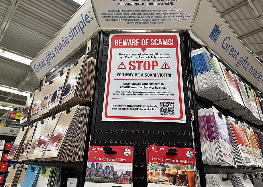 A large 'beware of scams' sign on display at a gift card aisle in a store. — melissamn // Shutterstock