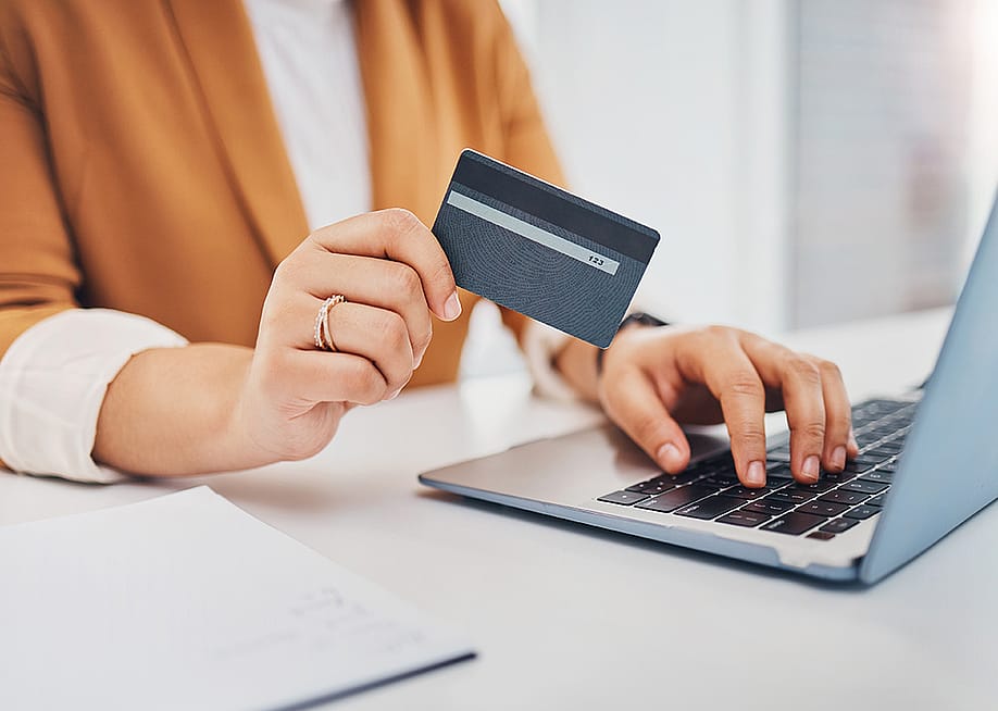 Person holding a credit card while using a laptop. — PeopleImages // Shutterstock