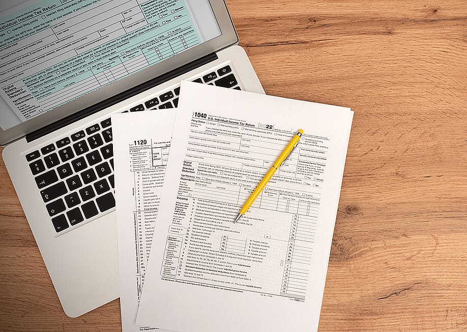 US tax form documents on top of a laptop. — Proxima Studio // Shutterstock