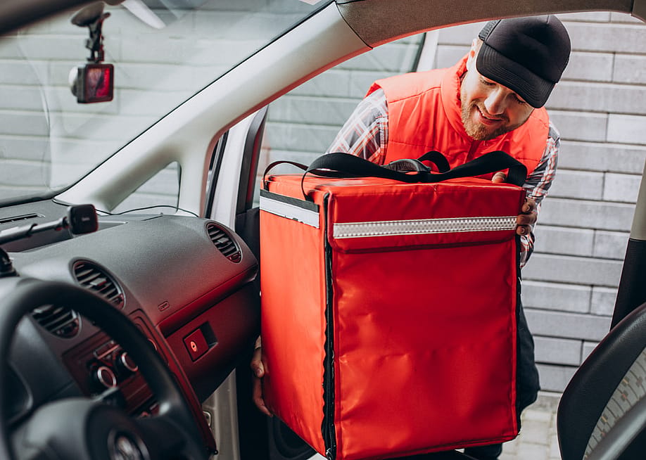 A food delivery person putting zipping up his delivery bag in his car. — PH888 // Shutterstock