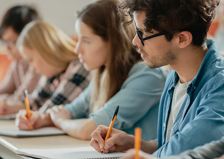 Teenage or young adult students seated in a row, taking notes. — Gorodenkoff // Shutterstock