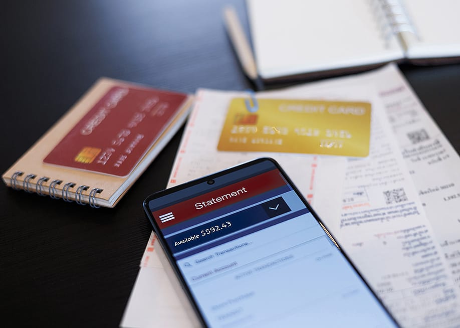 A close up on a credit card statement opened from a phone on top of physical credit cards and receipts. — Lek_charoen // Shutterstock
