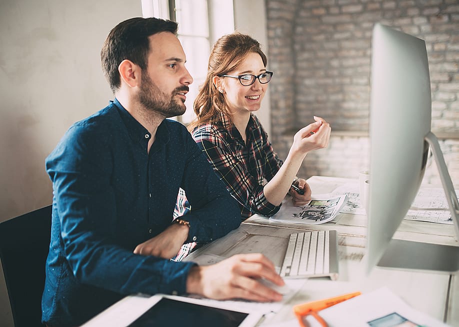 Two colleagues working in front of a computer monitor in an office. — NDAB Creativity // Shutterstock