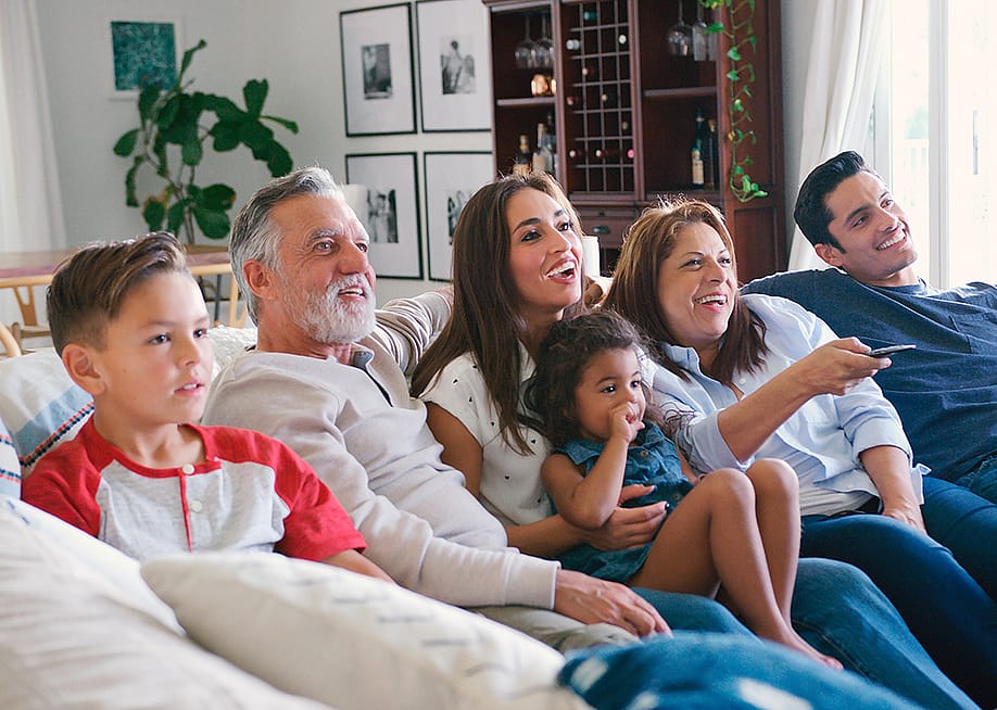 A multi-generational family sitting together on a sofa and watching televisions. — Monkey Business Images // Shutterstock