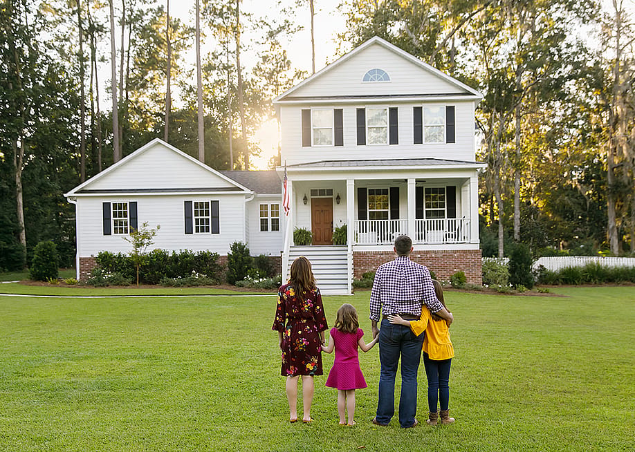 A family of four looking at their newly-constructed home. — Ursula Page // Shutterstock