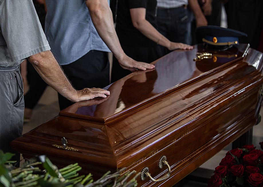 People touching the wooden brown coffin of a deceased relative. — Kirill_ak_ white // Shutterstock