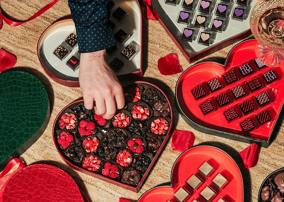 Person picking from a heart-shaped box of chocolates. — Compartés
