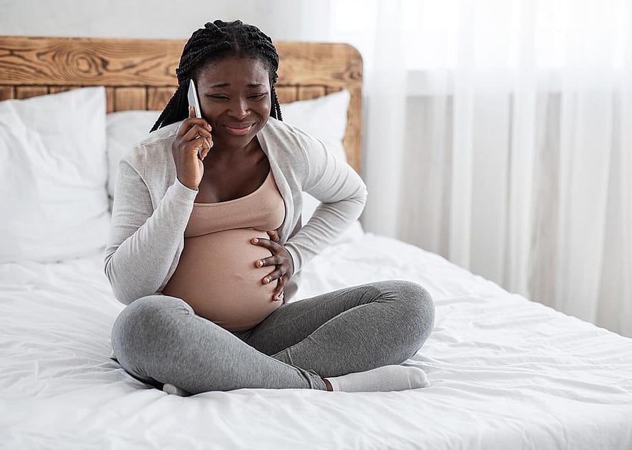 A pregnant young black woman calling on the phone while experiencing pain in her belly. — Prostock-studio // Shutterstock