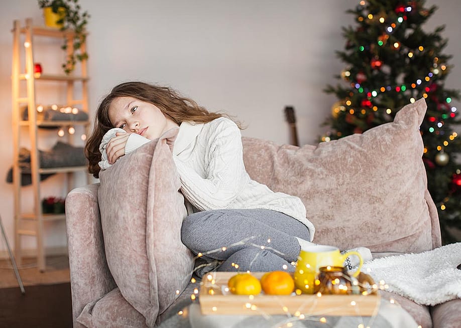 A sad young woman sitting on a sofa during the holidays. — Gladskikh Tatiana // Shutterstock