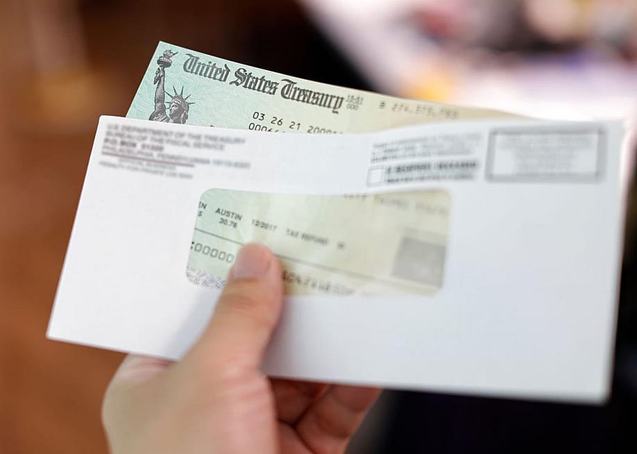 Person holding a tax refund check from government. — Bernie_Photo // Shutterstock