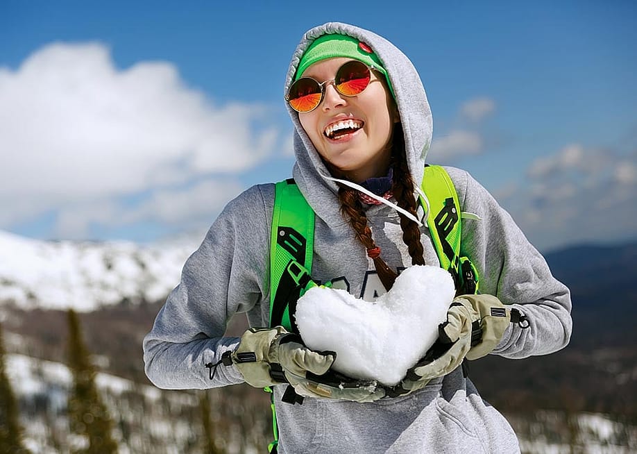 A young woman in snowboarding gear holding a heart shape made of snow. — Ipatov // Shutterstock