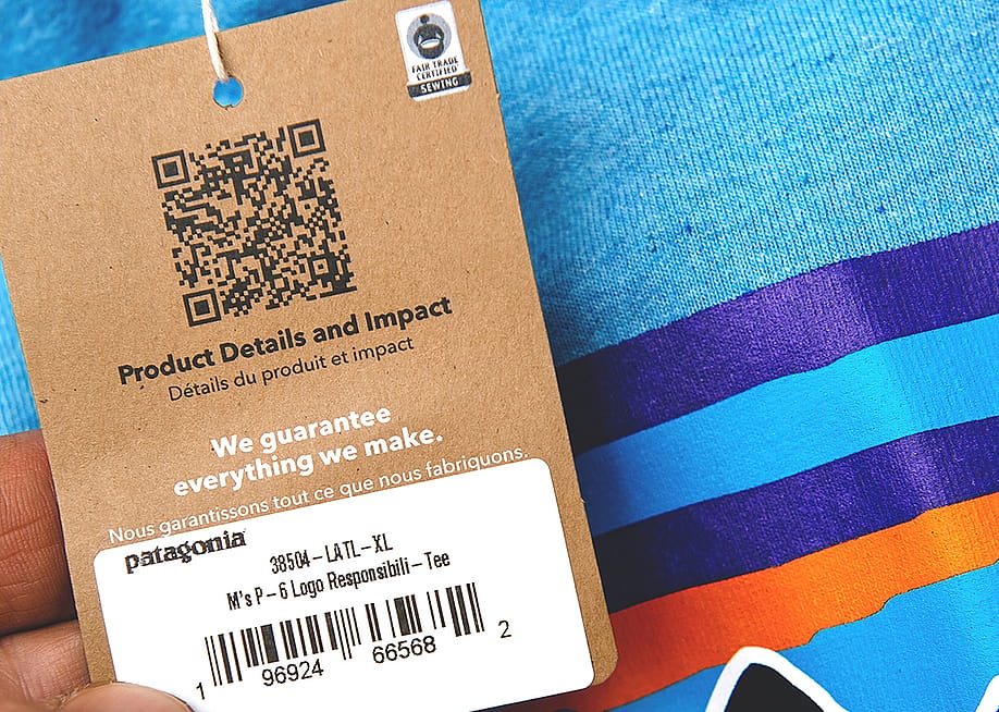 A product tag on a blue clothing shirt with QR code for product details and impact. — Hadrian // Shutterstock